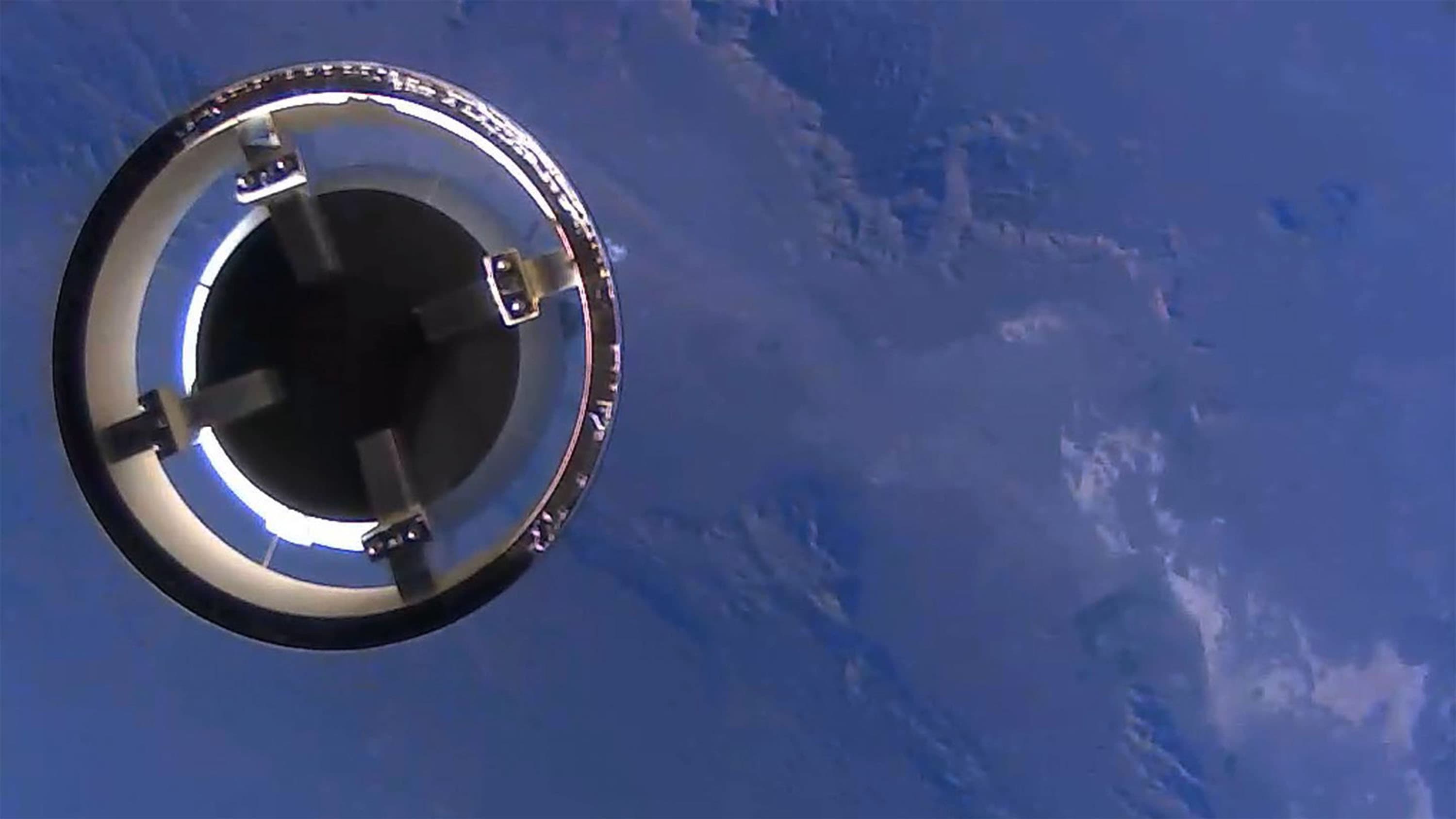 The open circular top of the booster floats in space, appearing against the blue background of Earth.