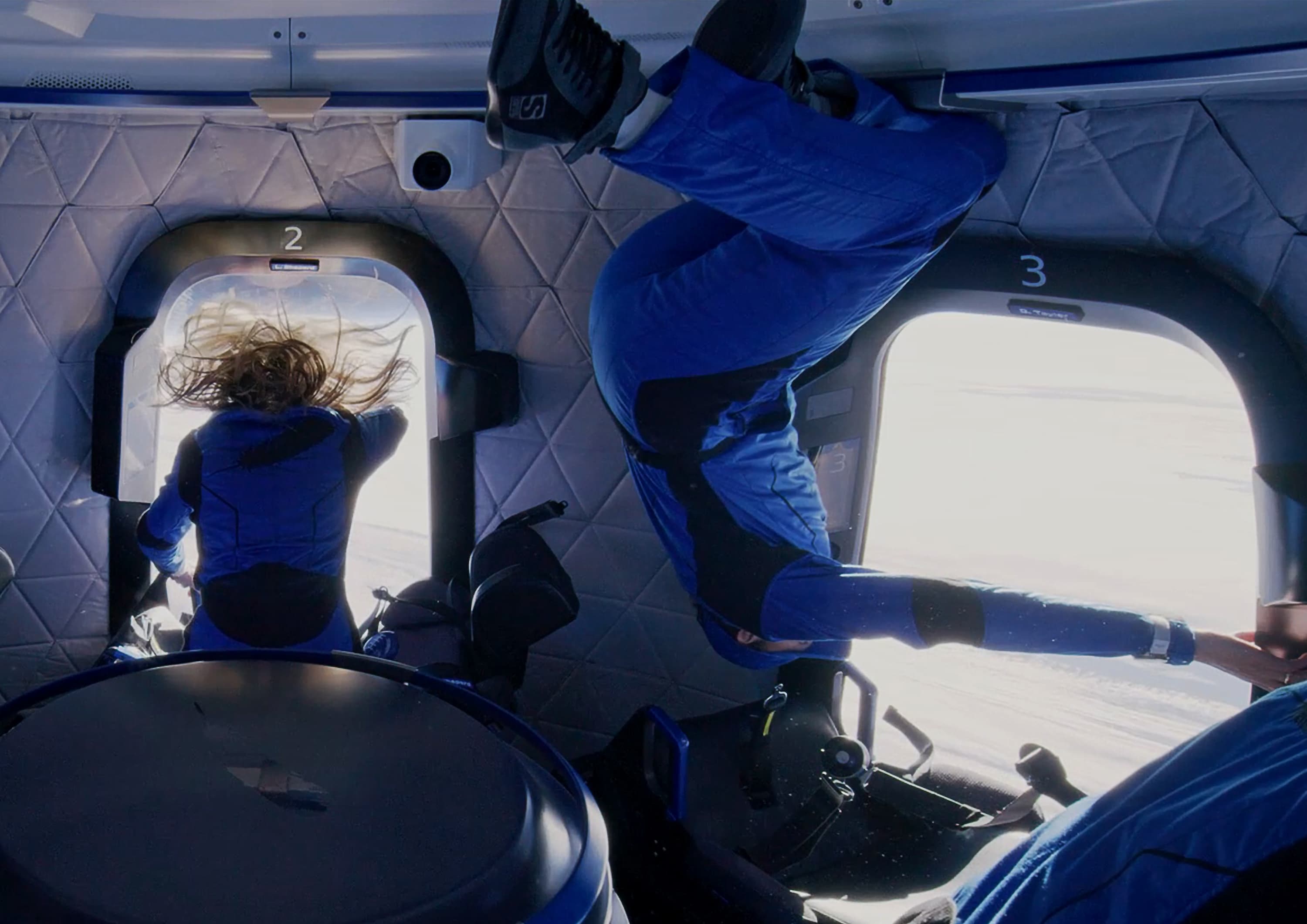 Laura floats upright and Dylan floats upside down while gazing out the windows at Earth.