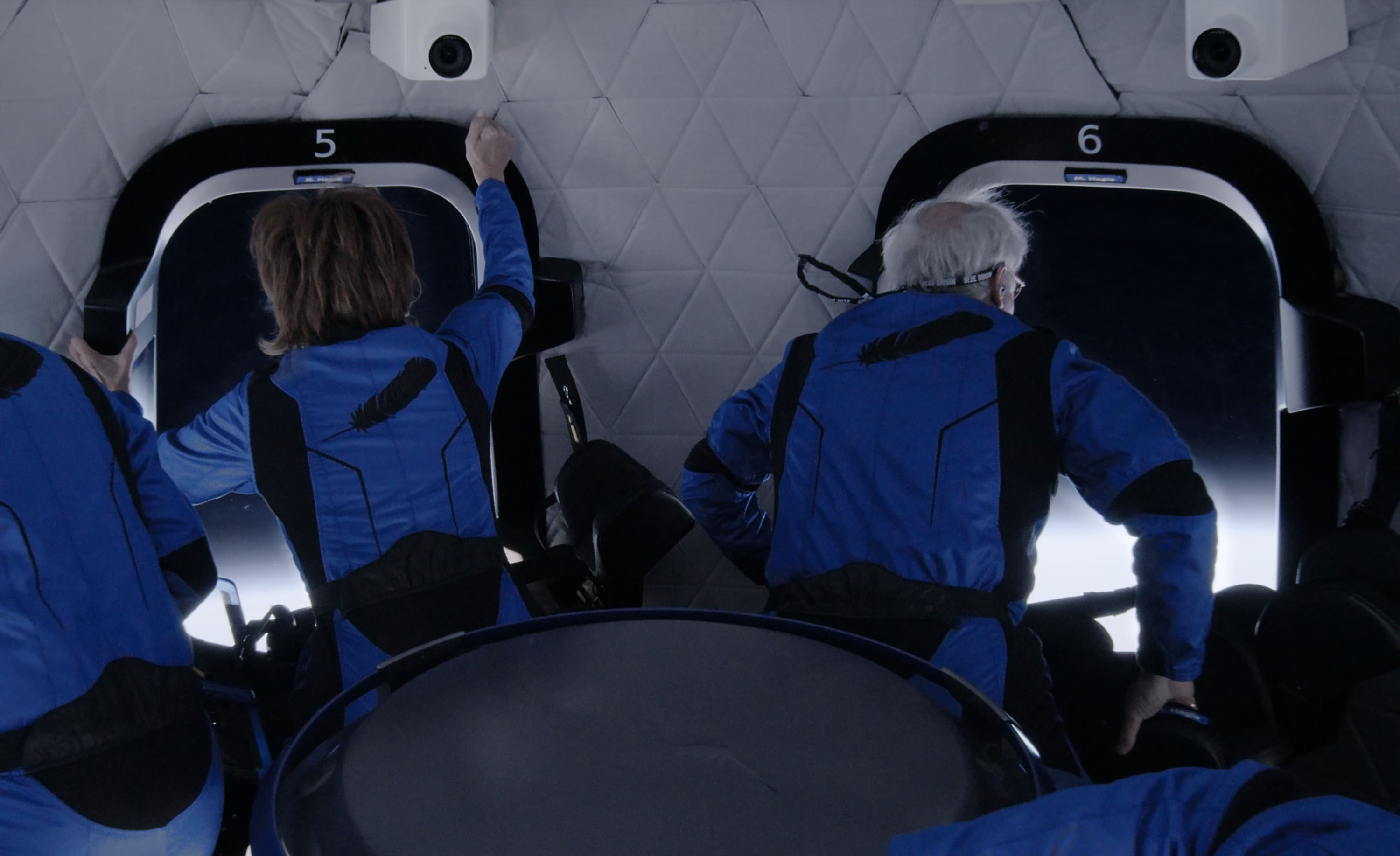 Sharon and Marc, with backs to camera, float inside the crew capsule and gaze out the windows into space.